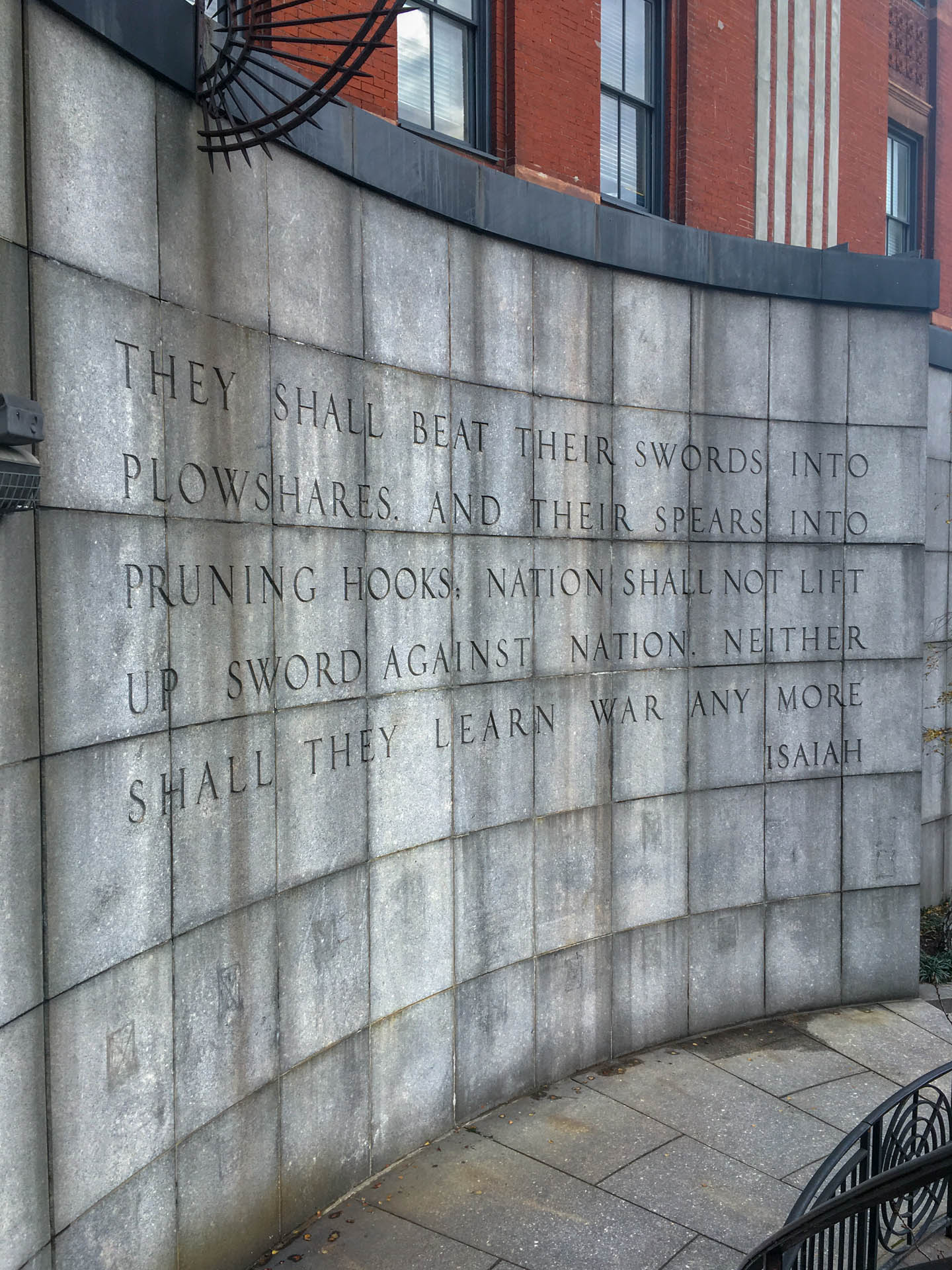 Stone wall with a quote inscribed that reads, "They shall beat their swords into plowshares and their spears into running hooks. National shall not lift up sword against nation. Neither shall they learn war any more." Isaiah